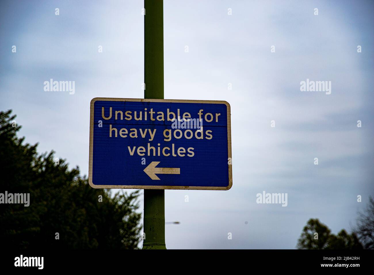 Dieses Bild eines für schwere Fahrzeuge ungeeigneten Schildes zeigt sein kräftiges Blau des Schildes selbst, inmitten seines unheimlichen launischen Himmels und Hintergrunds. Stockfoto