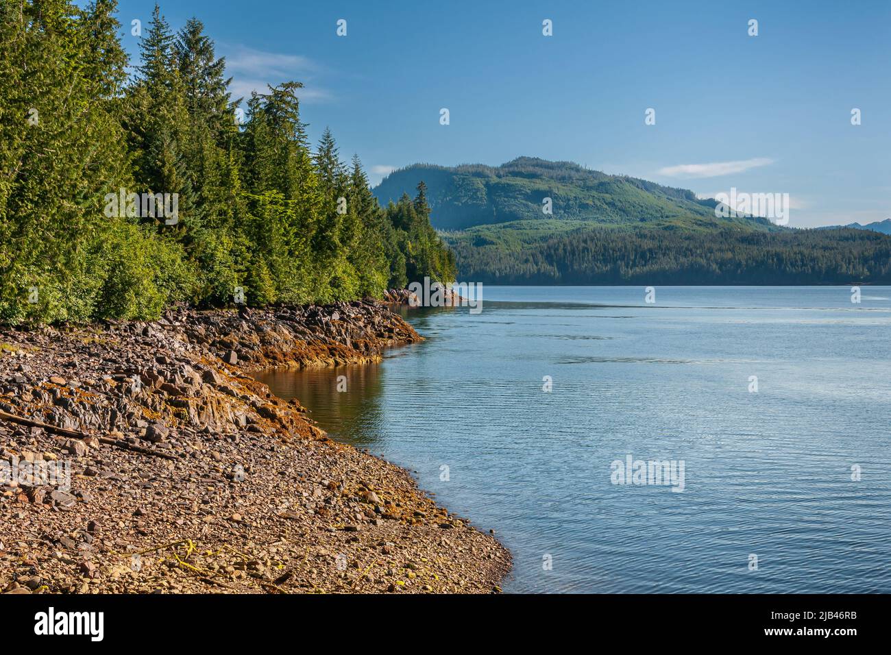 Ketchikan, Alaska, USA - 17. Juli 2011: Landschaft, dichte grüne Wälder über brauner Felsküste entlang der Tongass Narrows unter blauem Himmel. Berge an Stockfoto