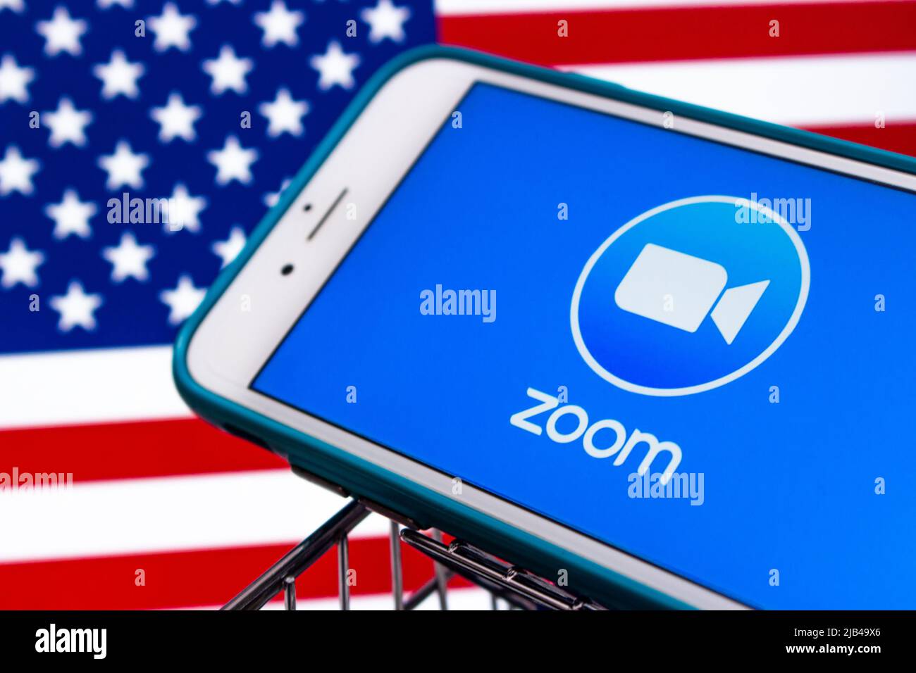 Logo der Zoom App, Videotelefonie- und Online-Chat-Dienste-App von Zoom Video Communications, Inc., auf dem iPhone im Warenkorb mit US-Flagge Stockfoto