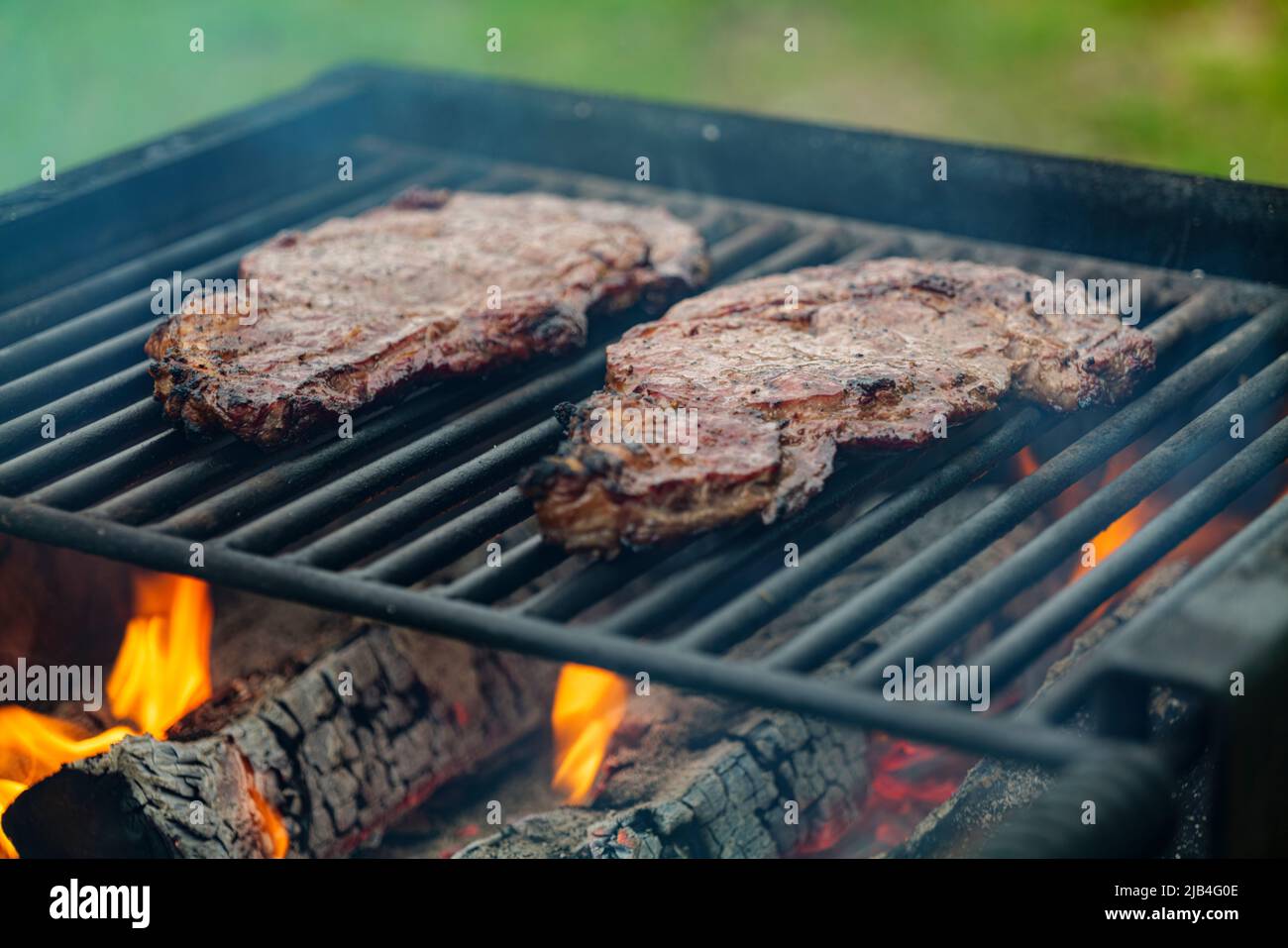 Selektiver Fokus auf saftige Rindersteaks beim Grillen auf Grillrost mit Rauch Stockfoto
