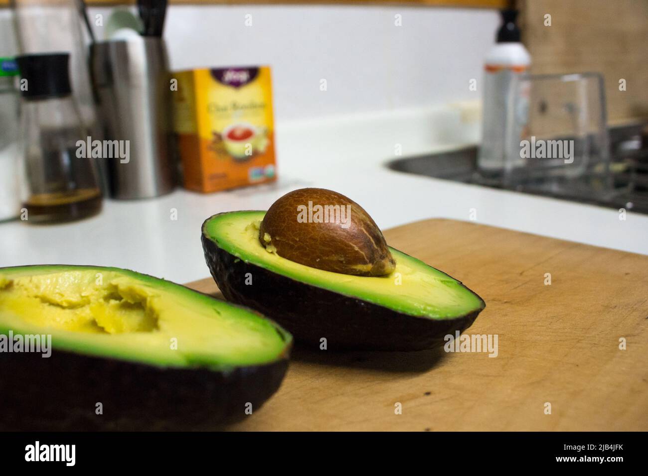 Ein einziger grüner Avocado, der in der Küche auf Holzschneidebrett halbiert wurde. Stockfoto