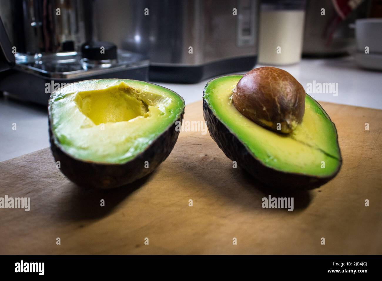 Ein einziger grüner Avocado, der in der Küche auf Holzschneidebrett halbiert wurde. Stockfoto