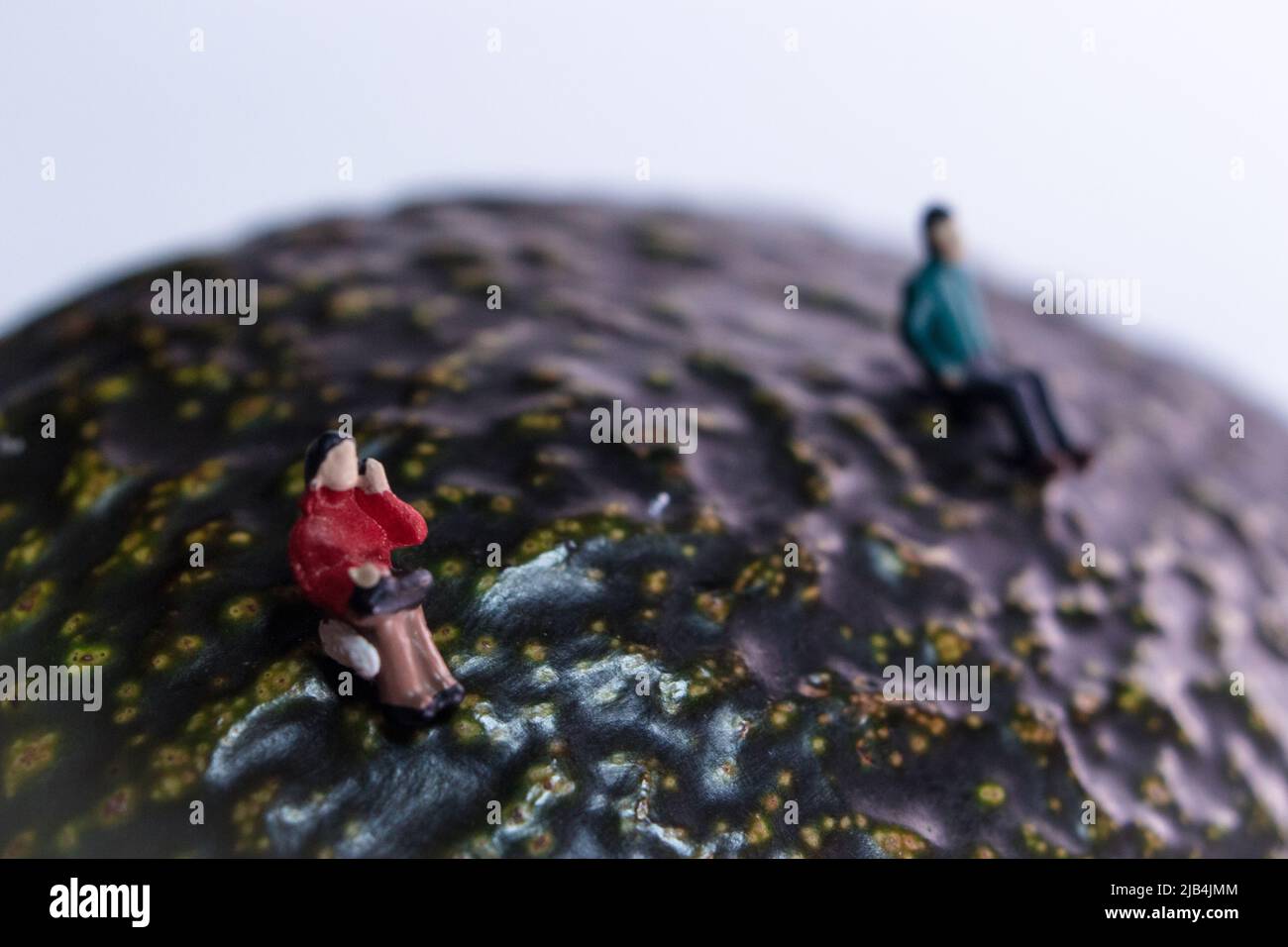 Eine Miniatur-Frau im roten Mantel, die auf einer Avocado (Alligatorbirne) sitzt. Die Frauen halten Abstand von dem Kerl. Stockfoto