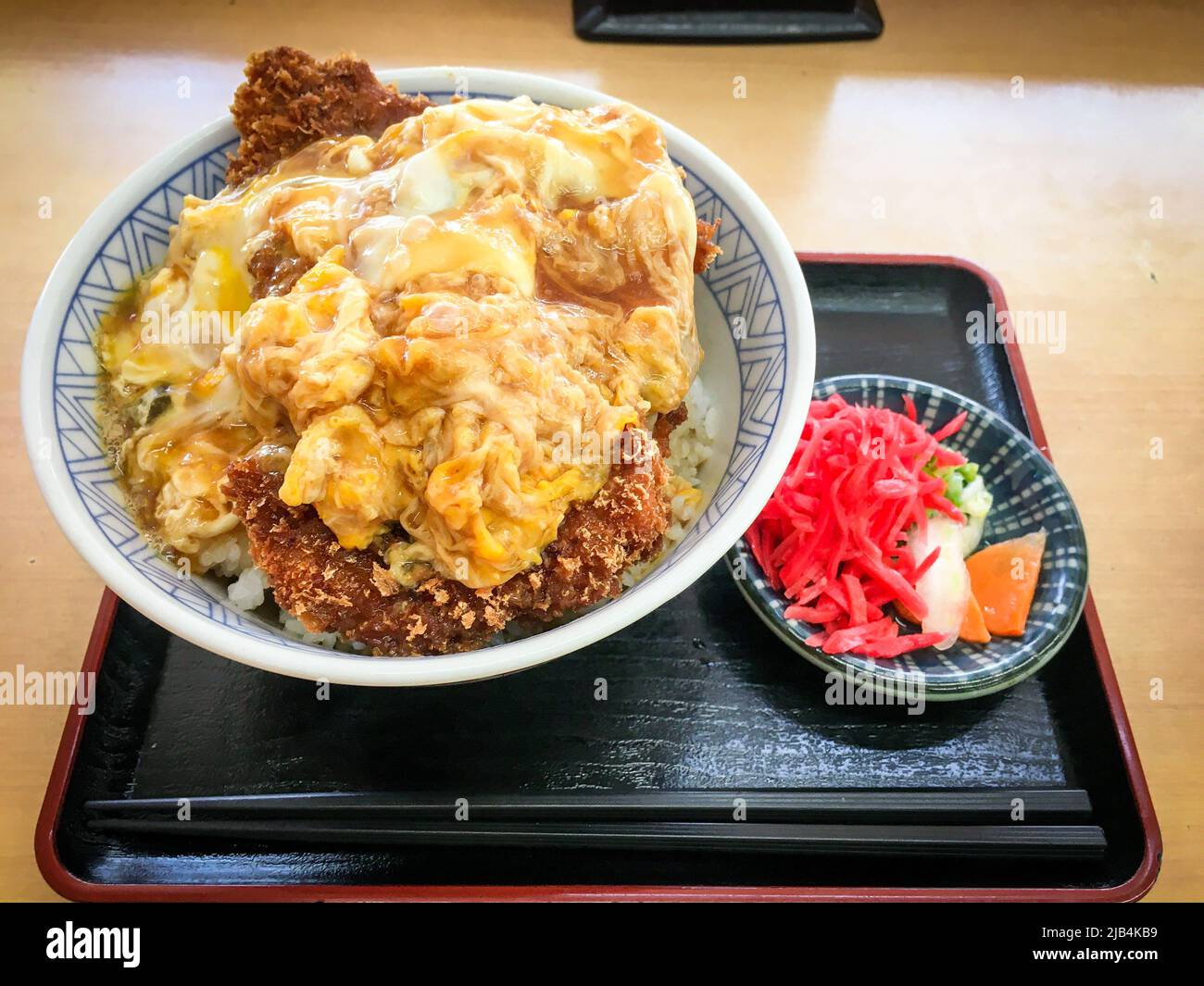 Katsudon, eine Schüssel Reis mit einem frittierten Schweineschnitzel, Ei, Gemüse und Gewürzen, mit Tsukemono-Gurken in einem lokalen Restaurant in Japan. Stockfoto