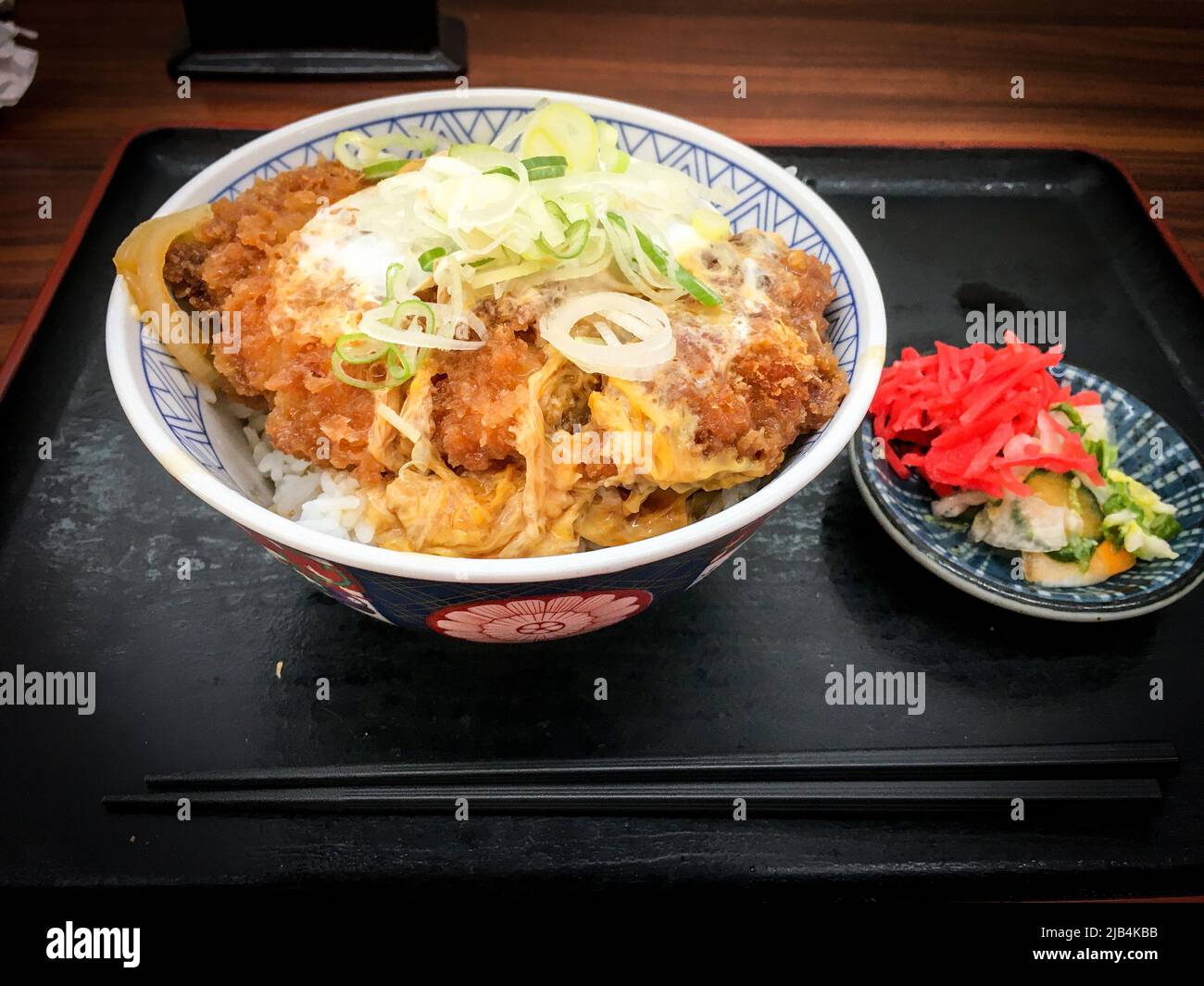 Katsudon, eine Schüssel Reis mit frittiertem Schweineschnitzel, Ei, Gemüse und Gewürzen, mit Tsukemono-Gurken auf einem Tisch im japanischen Restaurant Stockfoto