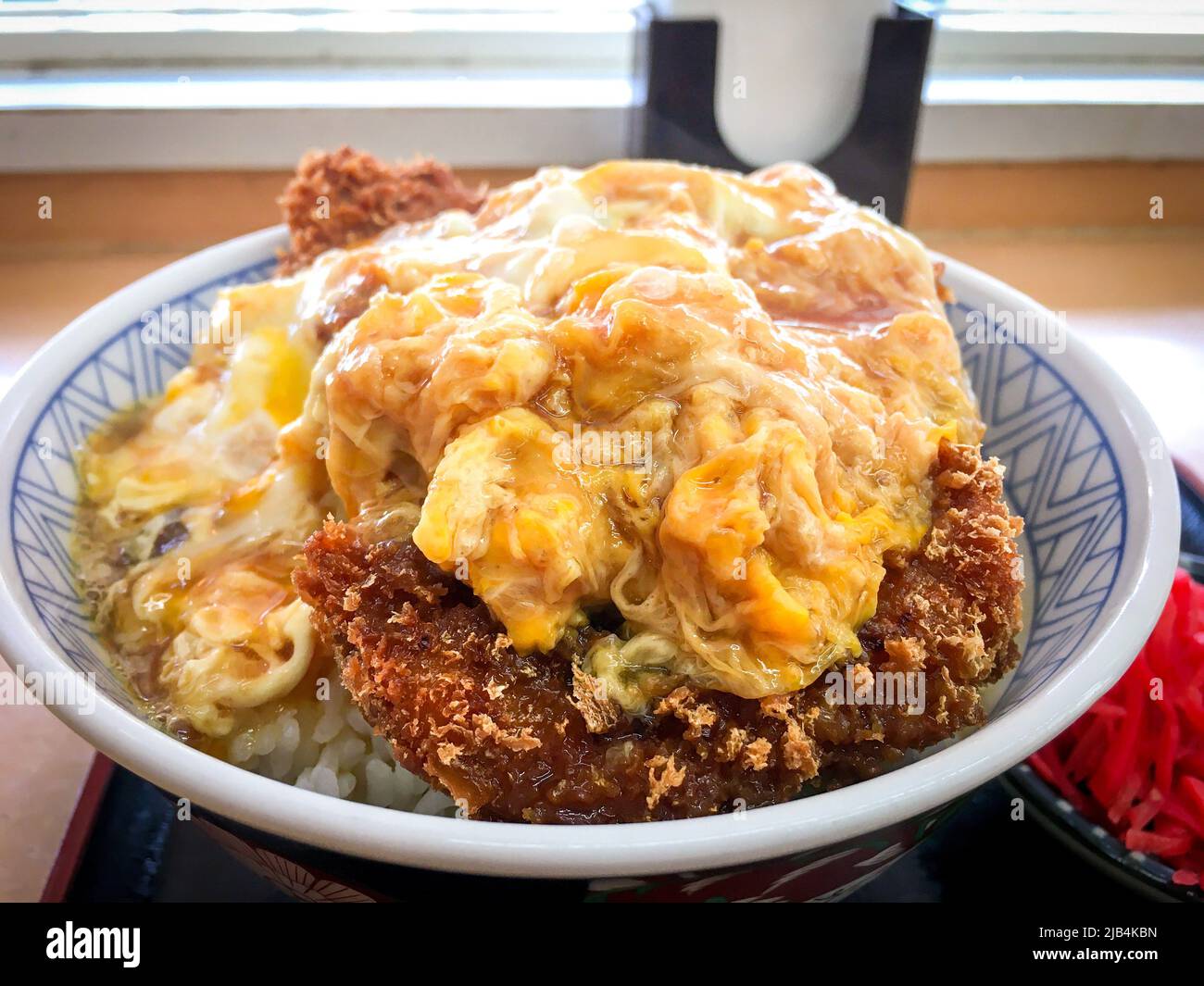 Katsudon, eine Schüssel Reis mit einem frittierten Schweineschnitzel, Ei, Gemüse und Gewürzen, mit Tsukemono-Gurken in einem lokalen Restaurant in Japan. Stockfoto