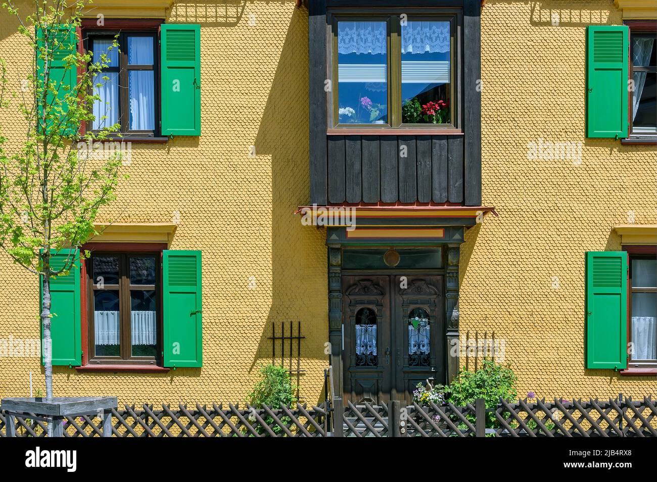 Gelbe Holzschindelfassade mit Erkerfenster und grünen Fensterläden, Oberstaufen, Allgäu, Bayern, Deutschland Stockfoto