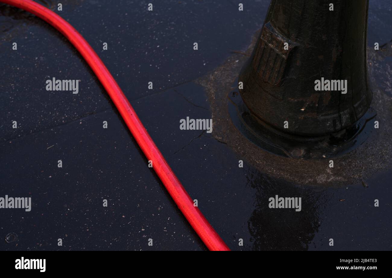 Roter Wasserschlauch auf nassem Asphalt, Lampenpfosten, Aix-en-Provence, Bouches-du-Rhone, Provence-Alpes-Cote d'Azur, Frankreich Stockfoto