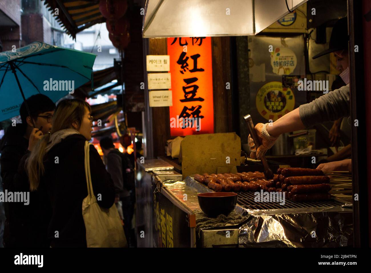 Jioufen, Taiwan - Dez 19 2019: Einkaufsstraße von Jioufen im Regen. Junges Paar neugierig Blick auf Take-out Wurst-Shop. Rote Bohnenkuchen (Radkuchen) Stockfoto