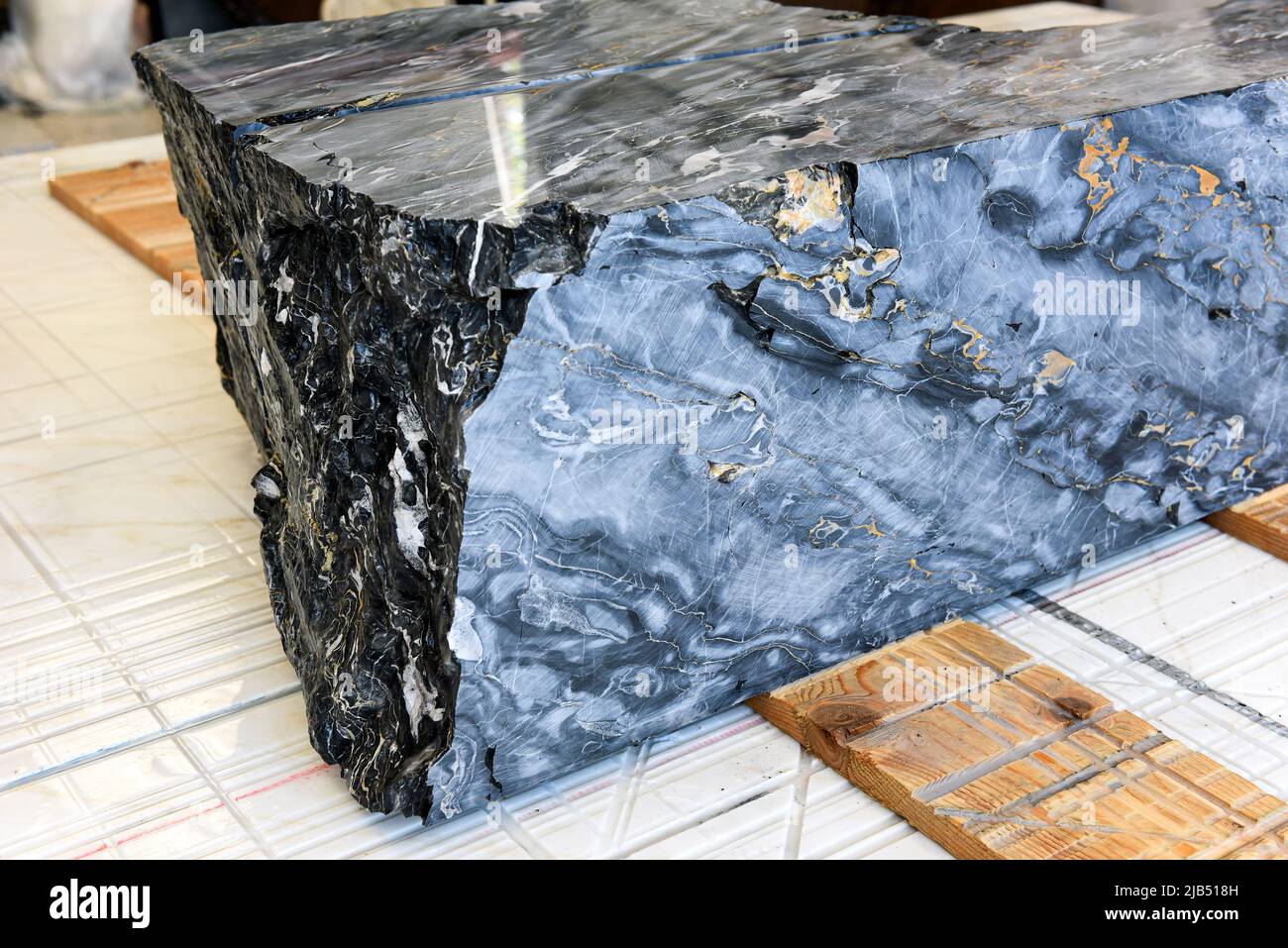 Hoher Winkel von großen Block aus schwarzem und Gold Portoro italienischen Marmor auf Holzbohlen auf Fliesenboden in der Werkstatt bereit geschnitten platziert werden Stockfoto