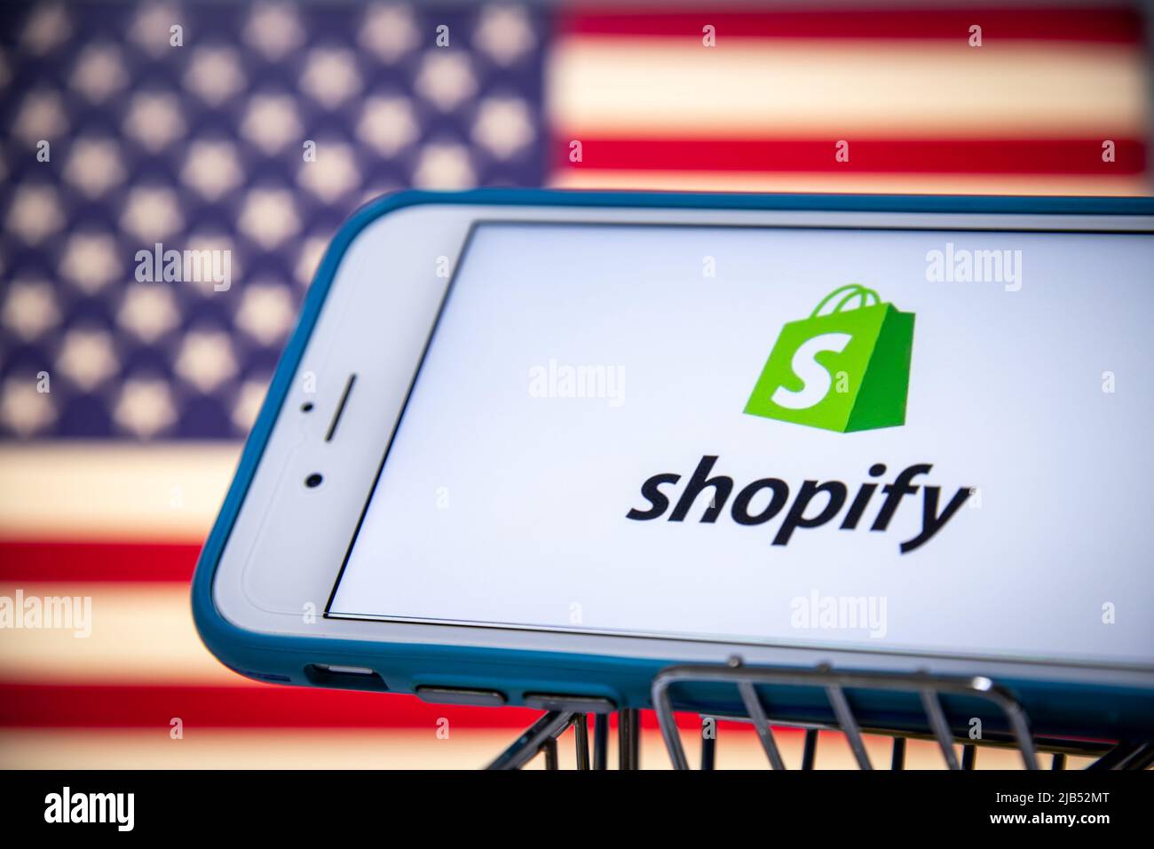 Logo von Shopify, einem kanadischen multinationalen E-Commerce-Unternehmen (Online-Shops und POS-Systeme für den Einzelhandel), auf dem iPhone im Einkaufswagen mit US-Flagge Stockfoto
