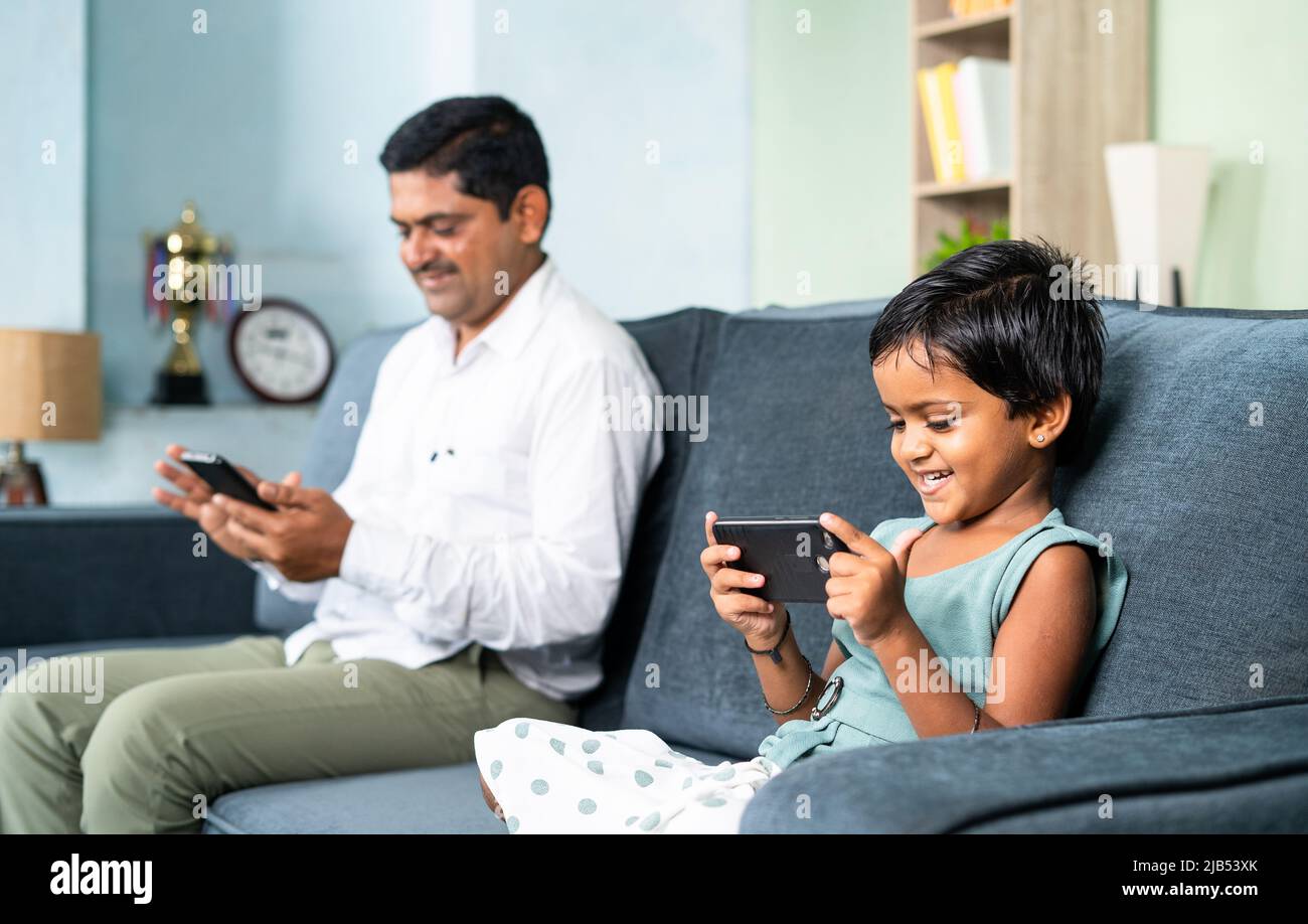 Vater und Tochter auf dem Sofa getrennt beschäftigt mit dem Handy zu Hause - Konzept der digitalen Spaltung, Social Media und Technologie sucht Stockfoto