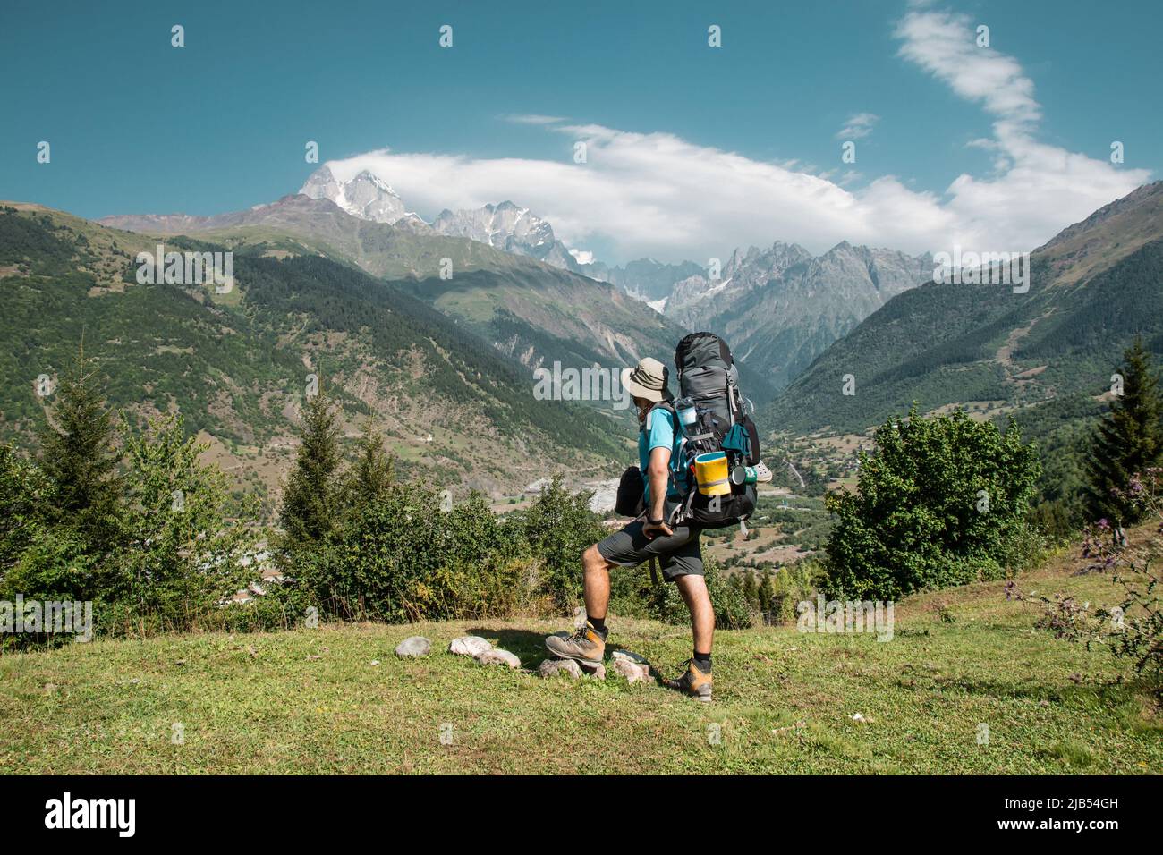 Wanderer Mann steht auf der Klippe gegen den Gipfel eines Berges. Der Mensch hat einen Rucksack und Wanderstöcke. Mountain Trekking. Platz kopieren Stockfoto
