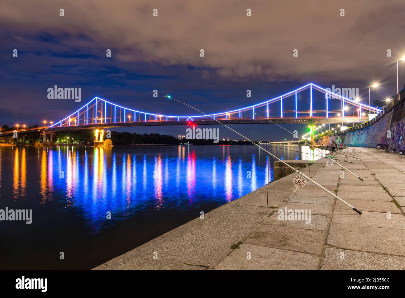 Nacht europäische Stadt in bunten Lichtern und Reflexion im Wasser, Kiew (Kiew) die Hauptstadt der Ukraine. Fußgängerbrücke über den Fluss Dnjepr und Vie Stockfoto