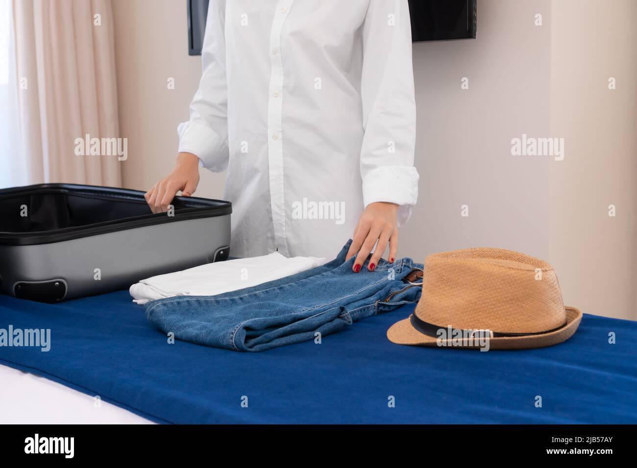 Frauenhände sammeln Dinge in einem Koffer, der auf dem Bett liegt. Frau in einem weißen Hemd sammelt Dinge in einem Koffer. Konzept von Tourismus, Reisen, Gepäck Stockfoto