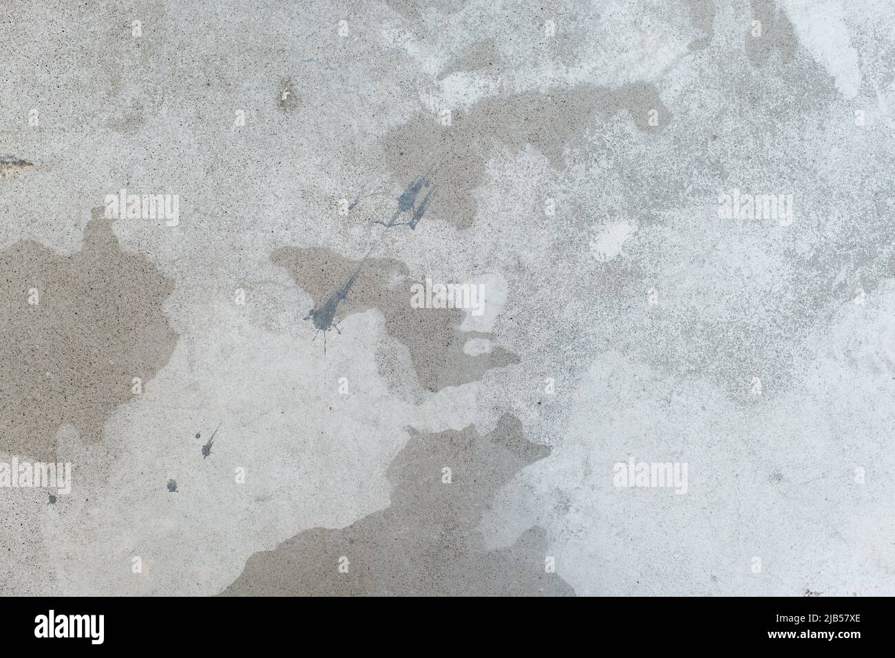 Weißer Spritzer auf grauer Betonwand, unordentliche, spritzige Oberfläche. Dekorative feuchte Farbtropfen, abstrakte Kunst Stockfoto