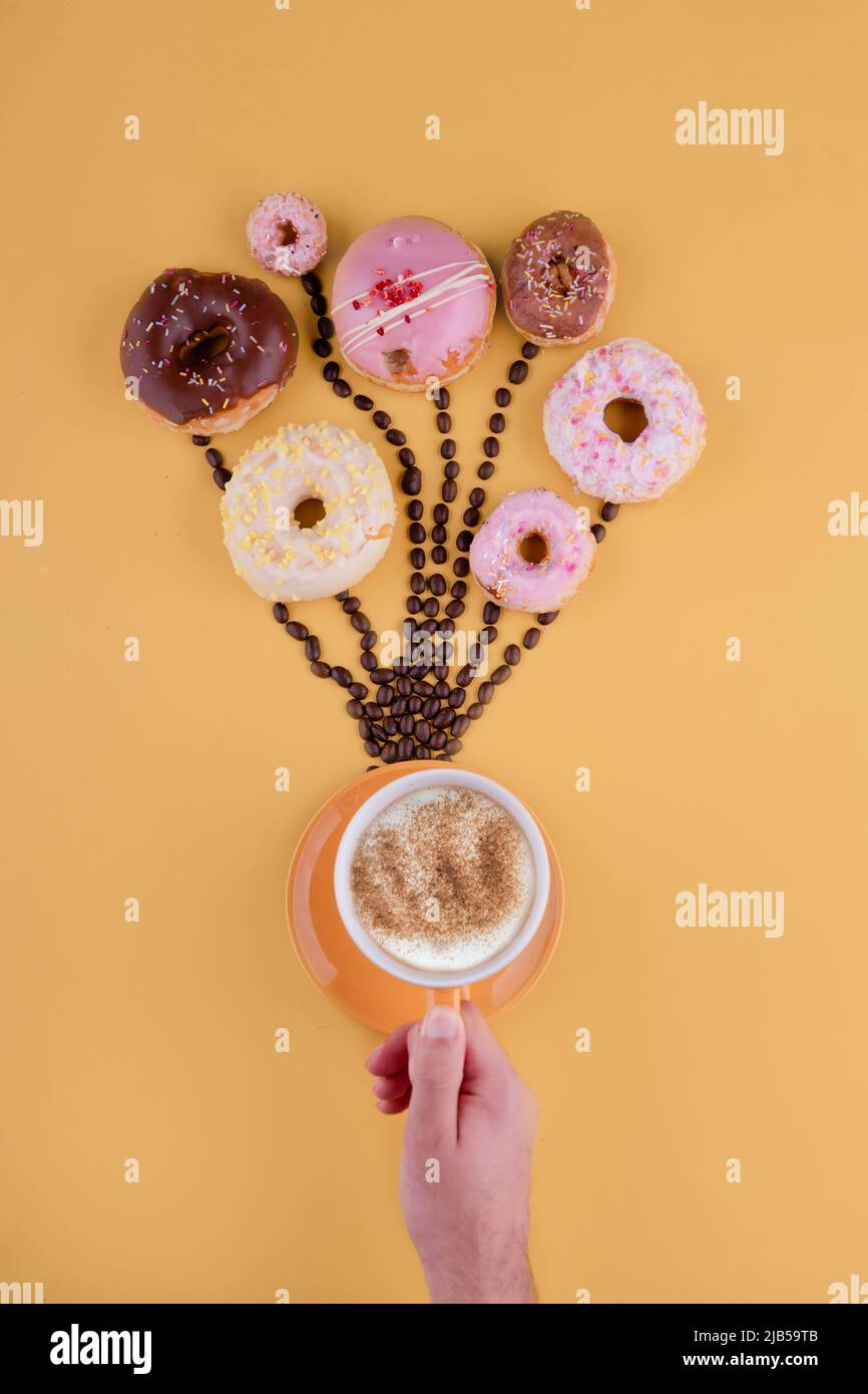 Verschiedene Donuts auf Kaffeebohnen wie Ballons auf gelbem Hintergrund Stockfoto