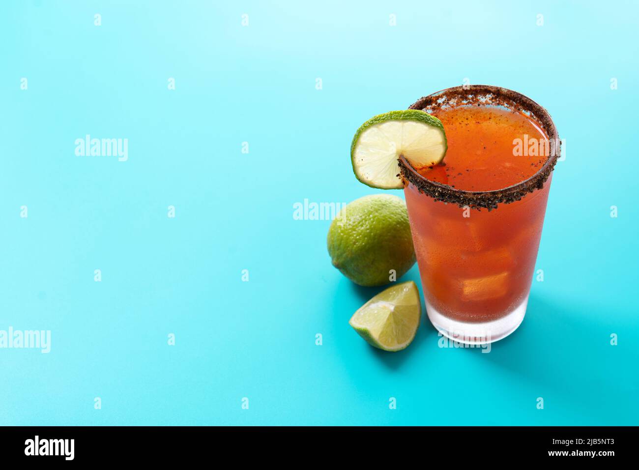 Hausgemachter Michelada-Cocktail mit Bier, Limettensaft, heißer Sauce, gesalzenem Rand und Tomatensaft auf blauem Hintergrund Stockfoto