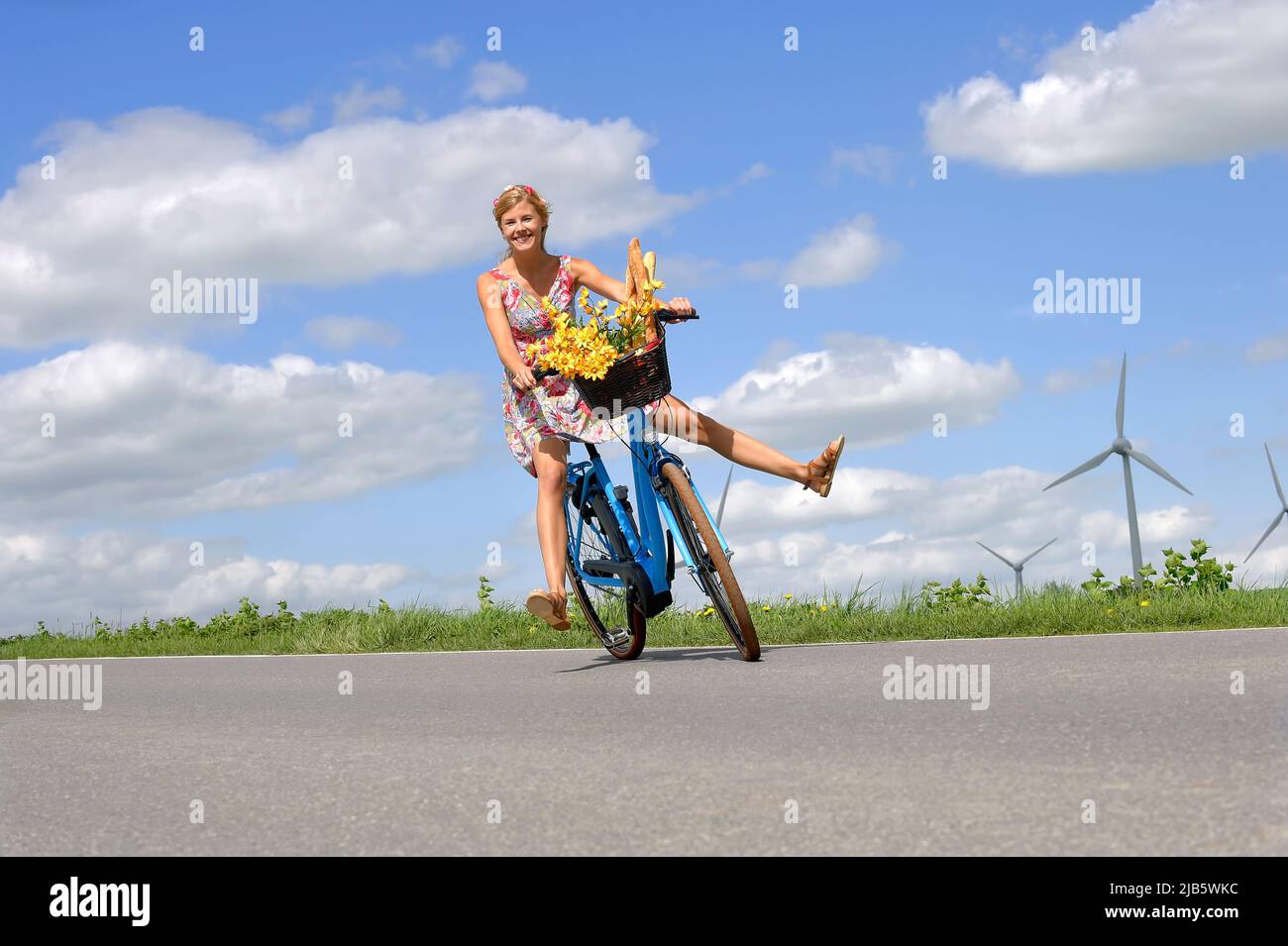 Eine unbeschwerte junge Frau genießt ihr neues Elektro-Hybrid-Fahrrad. Sie nimmt sich auf eine entspannte Fahrt auf dem Land, ohne ihre Fahrradpedale zu benutzen. Stockfoto