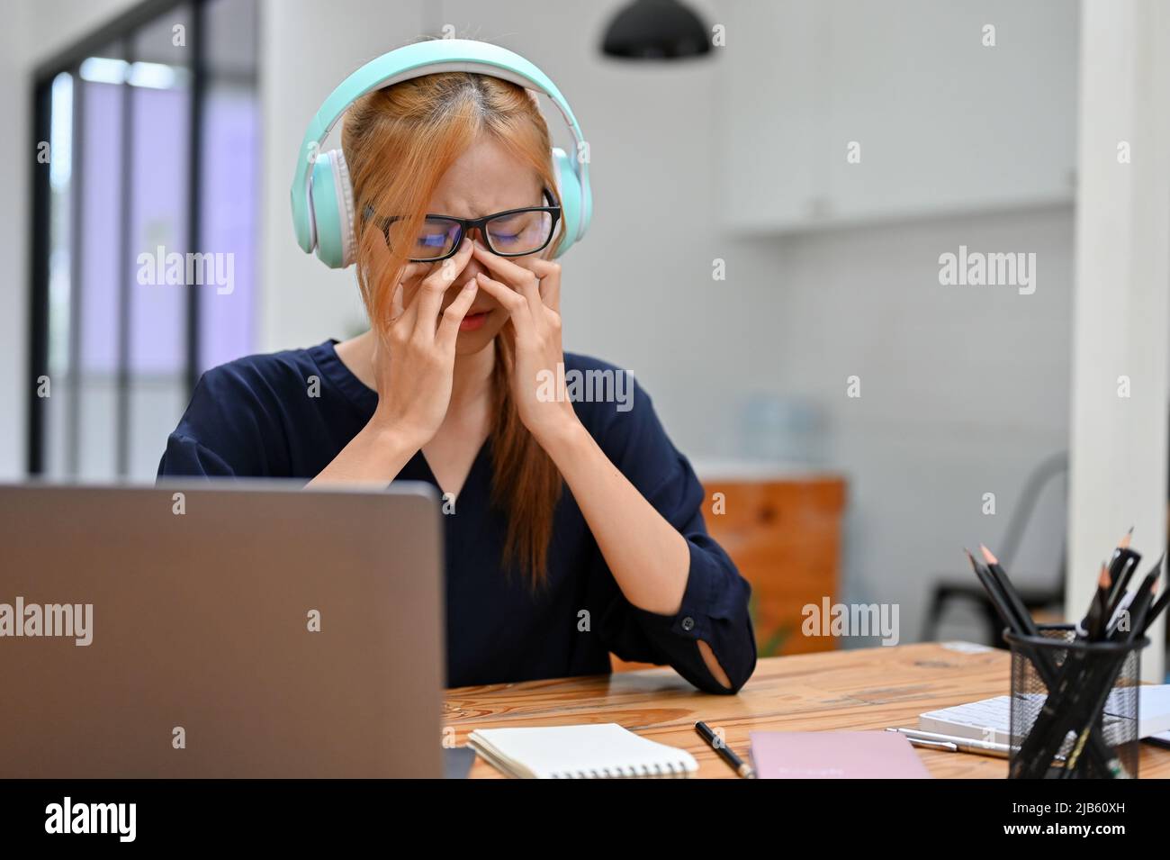 Traurige Teenager-Frau, die einen kabellosen Kopfhörer trägt und Musik vom Smartphone hört, während sie in ihrem Arbeitsplatz sitzt. Verärgert, gescheitert, niedergeschlagen. Stockfoto