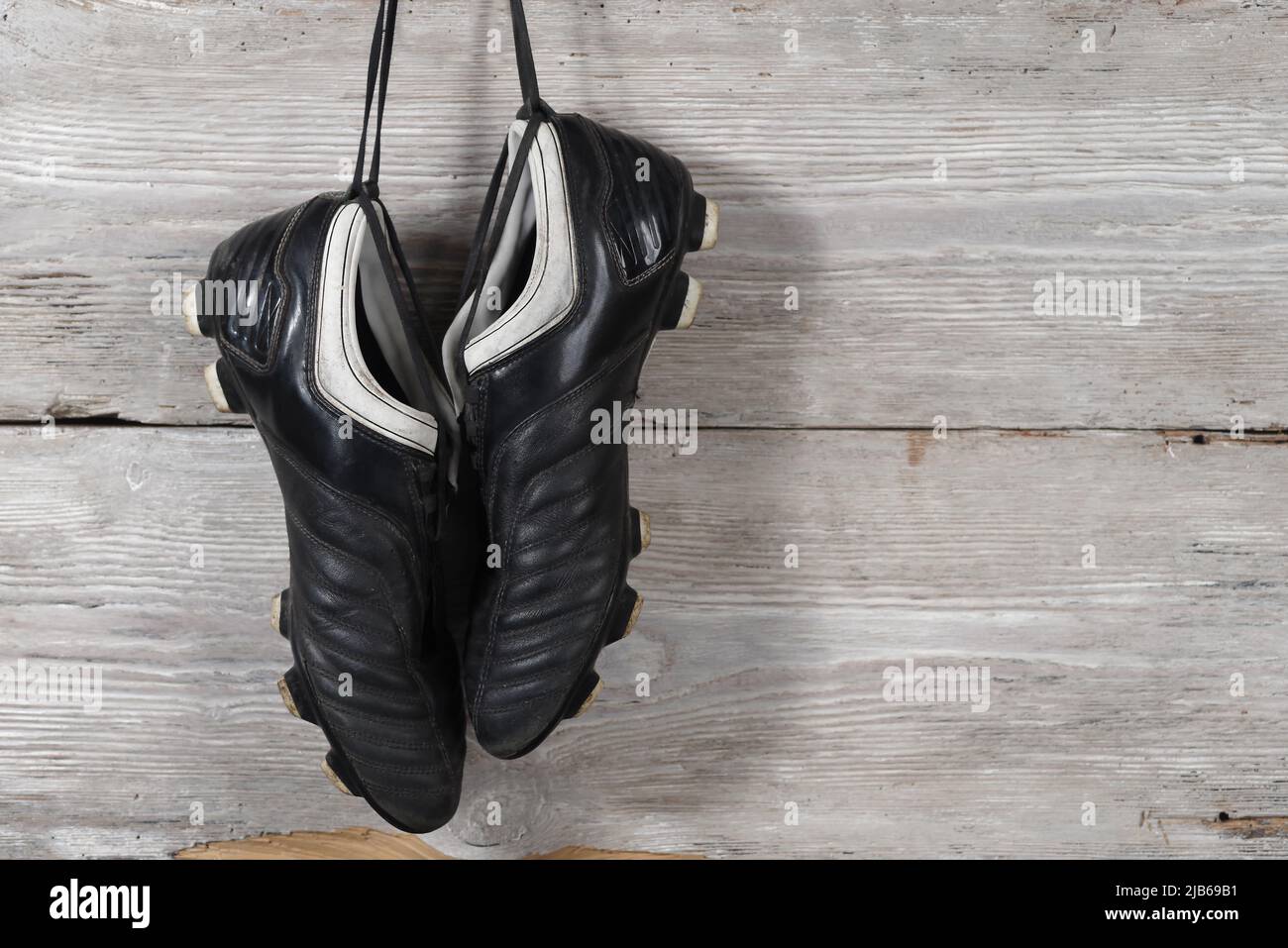 Ein Paar Fußballschuhe, die an einer Holzwand hängen. Das Ende der Fußballkarriere Stockfoto