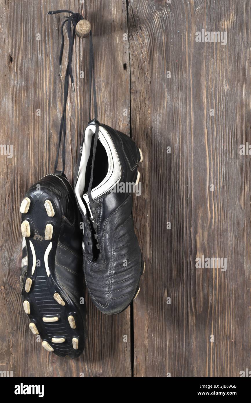 Ein Paar Fußballschuhe, die an einer Holzwand hängen. Das Ende der Fußballkarriere Stockfoto