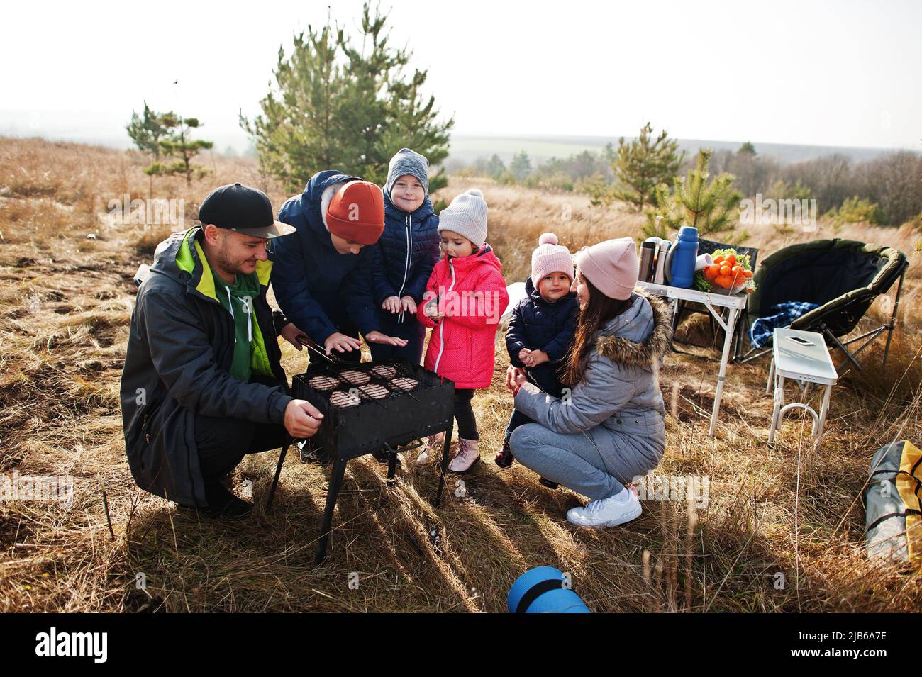 Große Familie mit vier Kindern grillen auf einer Terrasse im Pinienwald. Grilltag mit Grill. Stockfoto