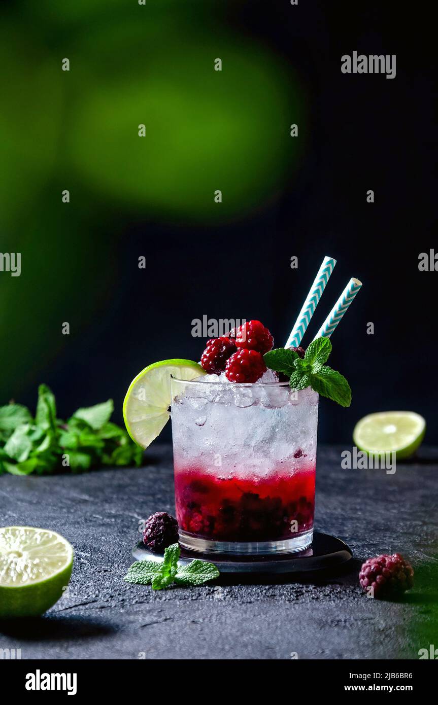 Cocktail mit Rum oder Vodka, Soda, Himbeer- und Brombeerpüree, Limette und Minze im Glas auf dem dunkelgrauen Hintergrund Stockfoto