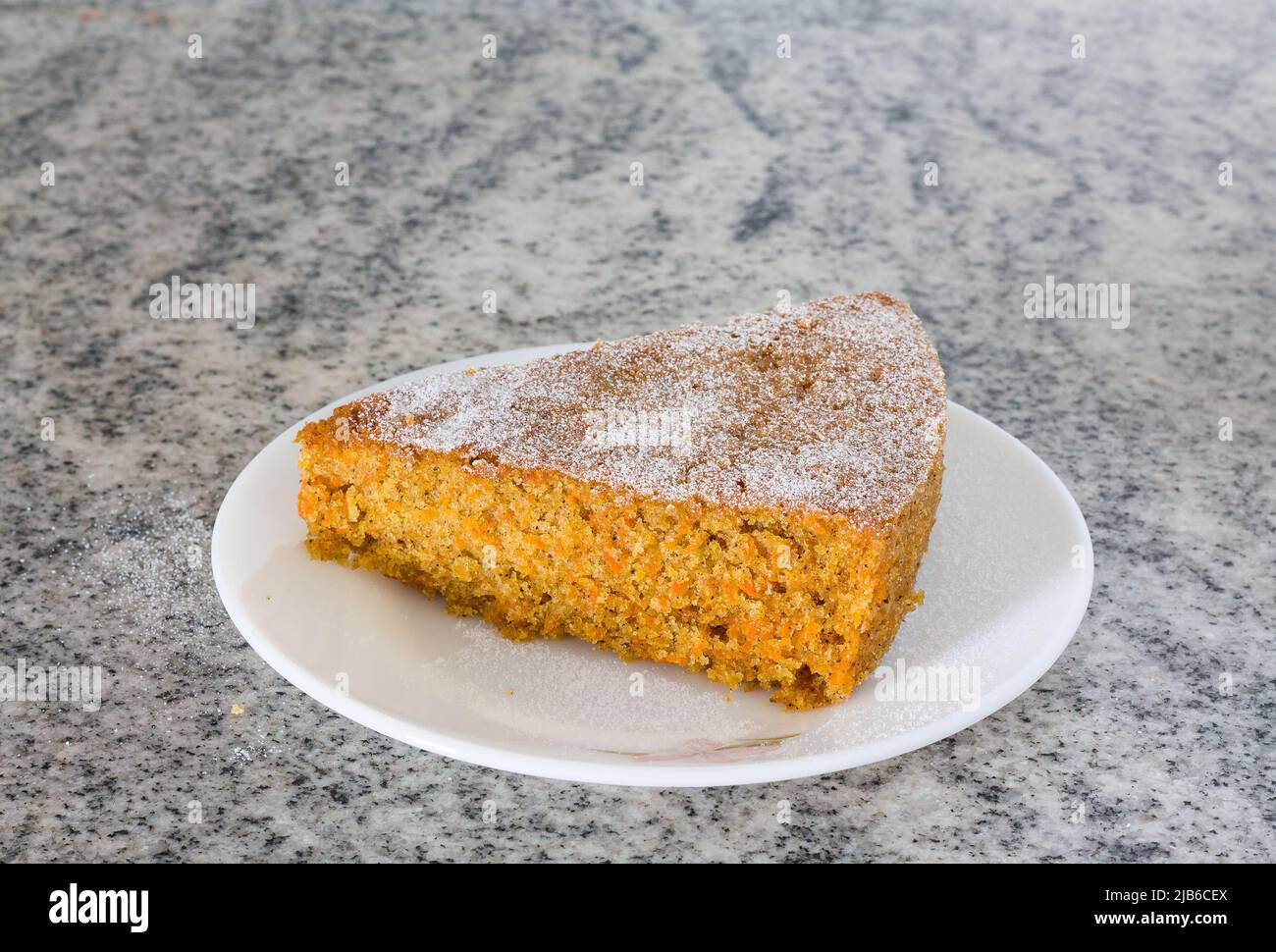 Vorderansicht, Nahaufnahme eines Stücks frischer Karottenkuchen mit Puderzucker bestreut auf weißem Marmorhintergrund. Feuchter, hausgemachter Weihnachtskuchen. Stockfoto