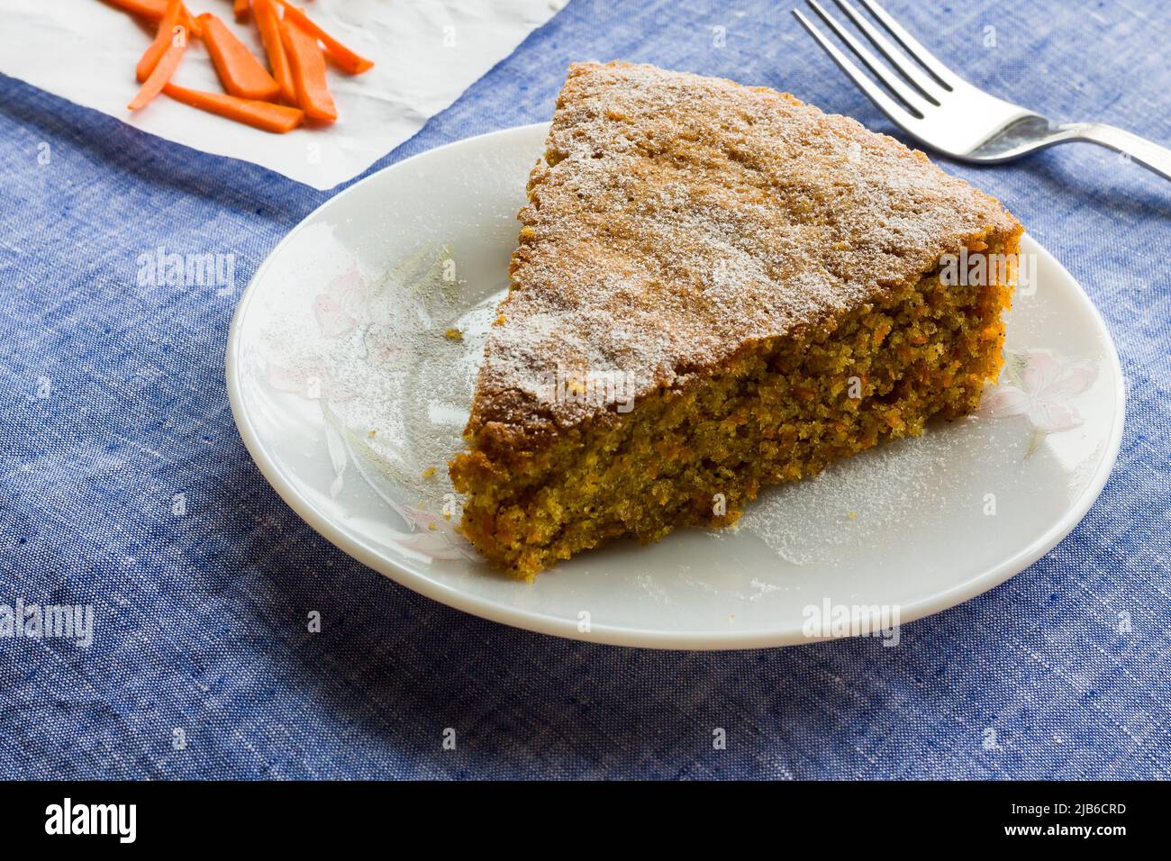 Nahaufnahme der Scheibe frischer Karottenkuchen mit Puderzucker bestreut oben, auf dunkelblauem Hintergrund platziert. Feuchter, hausgemachter, weicher Sommerteekuchen. Stockfoto