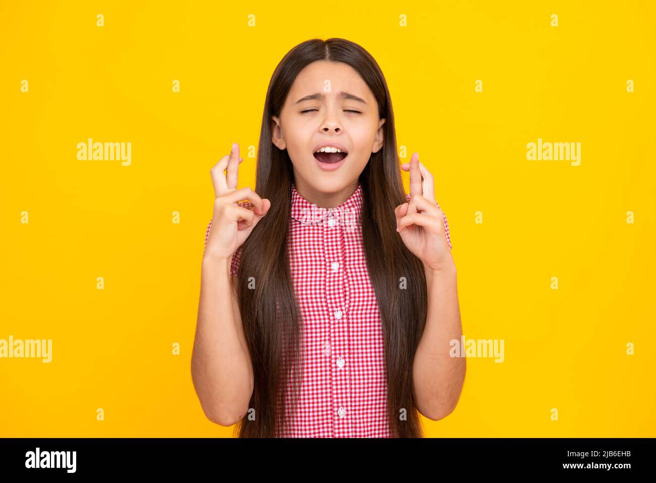 Froh Teenager-Mädchen kreuzt die Finger, schließt die Augen mit Vergnügen, erwarten hören gute Nachrichten, isolierten gelben Hintergrund. Glückliches Kind freut sich, dass seine Stockfoto
