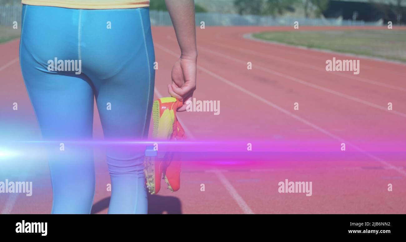 Bild von Licht, das sich über den mittleren Bereich der Frau bewegt, die Laufschuhe in der Hand hält und auf der Laufstrecke läuft Stockfoto