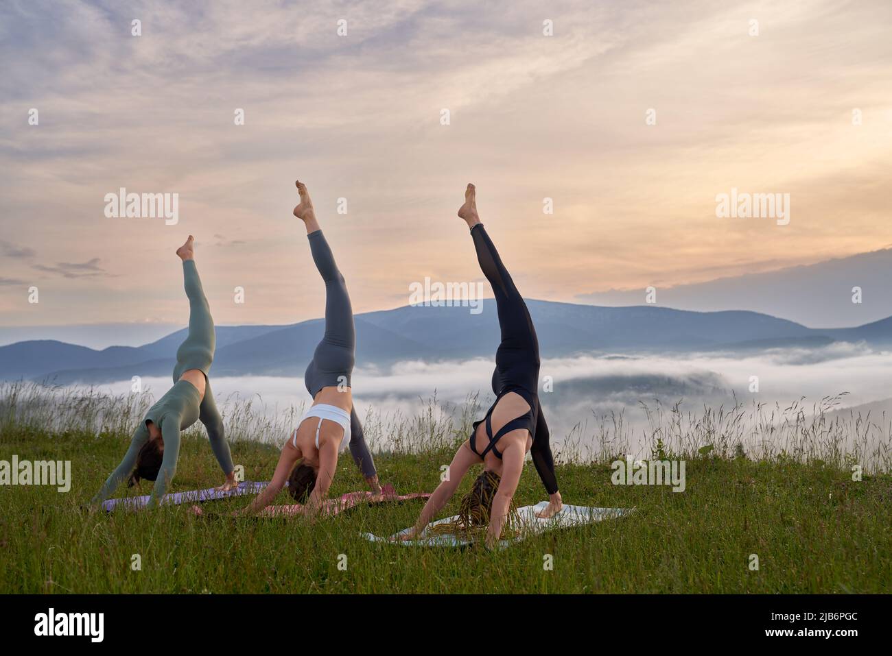 Eine Gruppe von drei jungen Frauen in Sportkleidung, die Yoga üben und dabei einen atemberaubenden Blick auf die Berge haben. Konzept der Menschen, Training und gesunde Lebensweise. Stockfoto