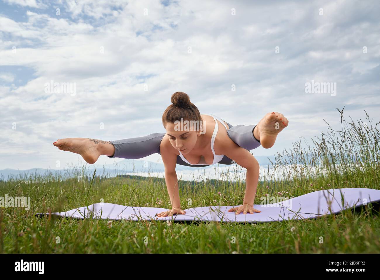 Starke junge Frau im aktiven Ohr balanciert auf den Händen und dehnt die Beine während der Freizeit an der frischen Luft. Konzept eines gesunden und aktiven Lebensstils. Stockfoto