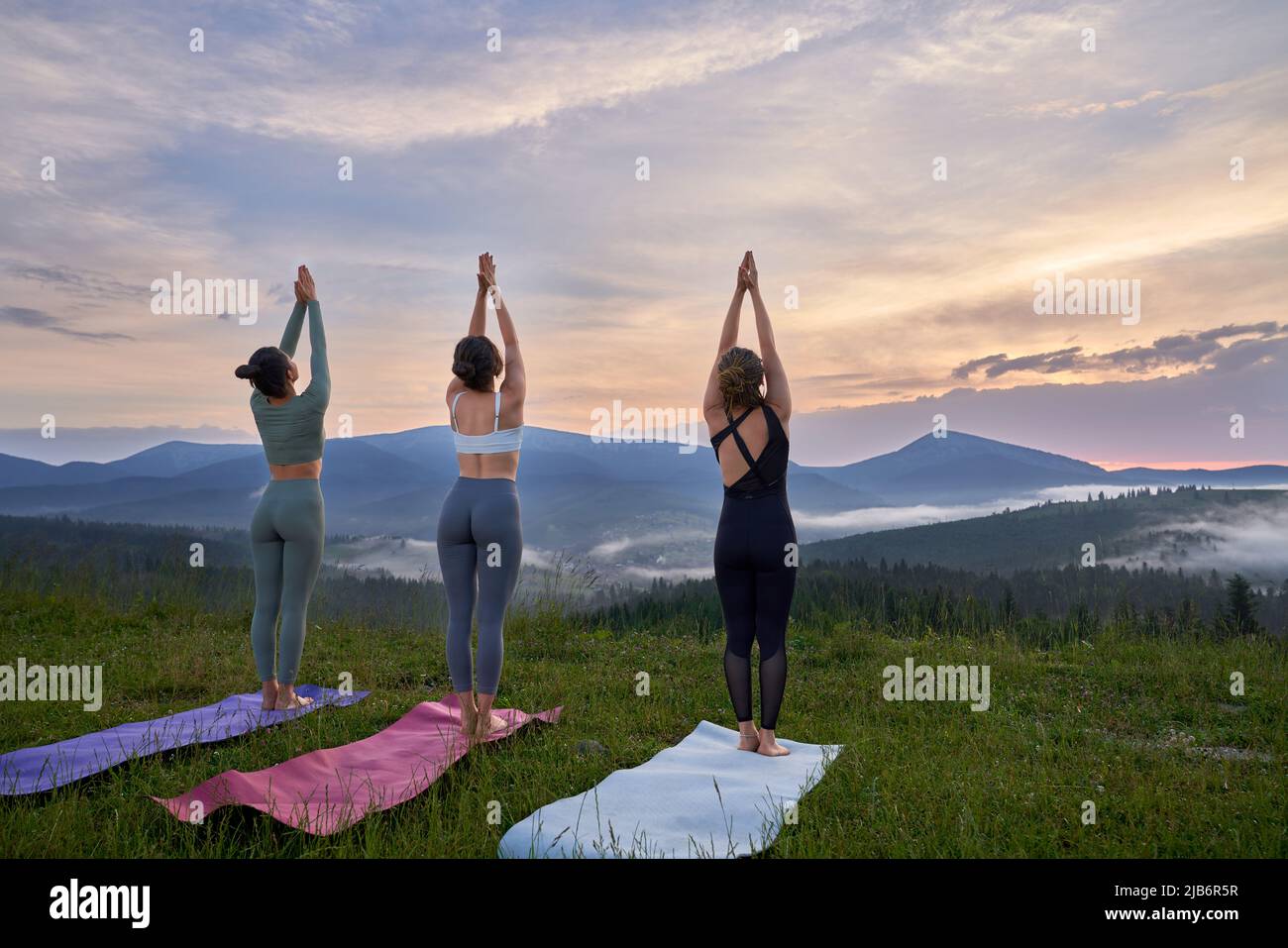 Rückansicht von drei Fitness-Frauen in Sportkleidung, die in der Freizeit Meditation im Freien genießen. Konzept der Menschen, Training und eine gesunde Lebensweise. Stockfoto
