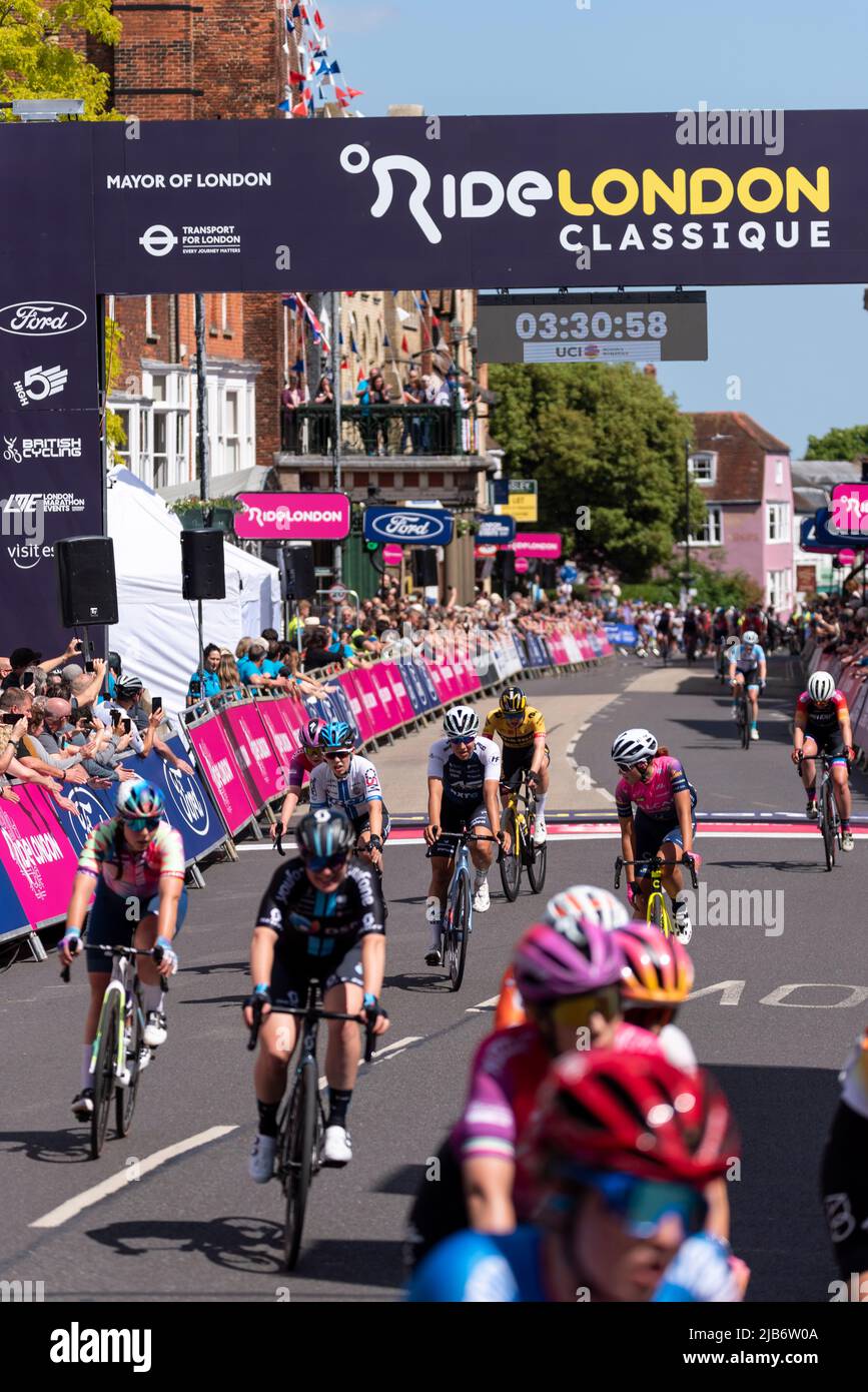 Radsportler des Pelotons überqueren die Ziellinie in der Maldon High Street beim Radrennen RideLondon Classique Stage 1, Essex, Großbritannien Stockfoto