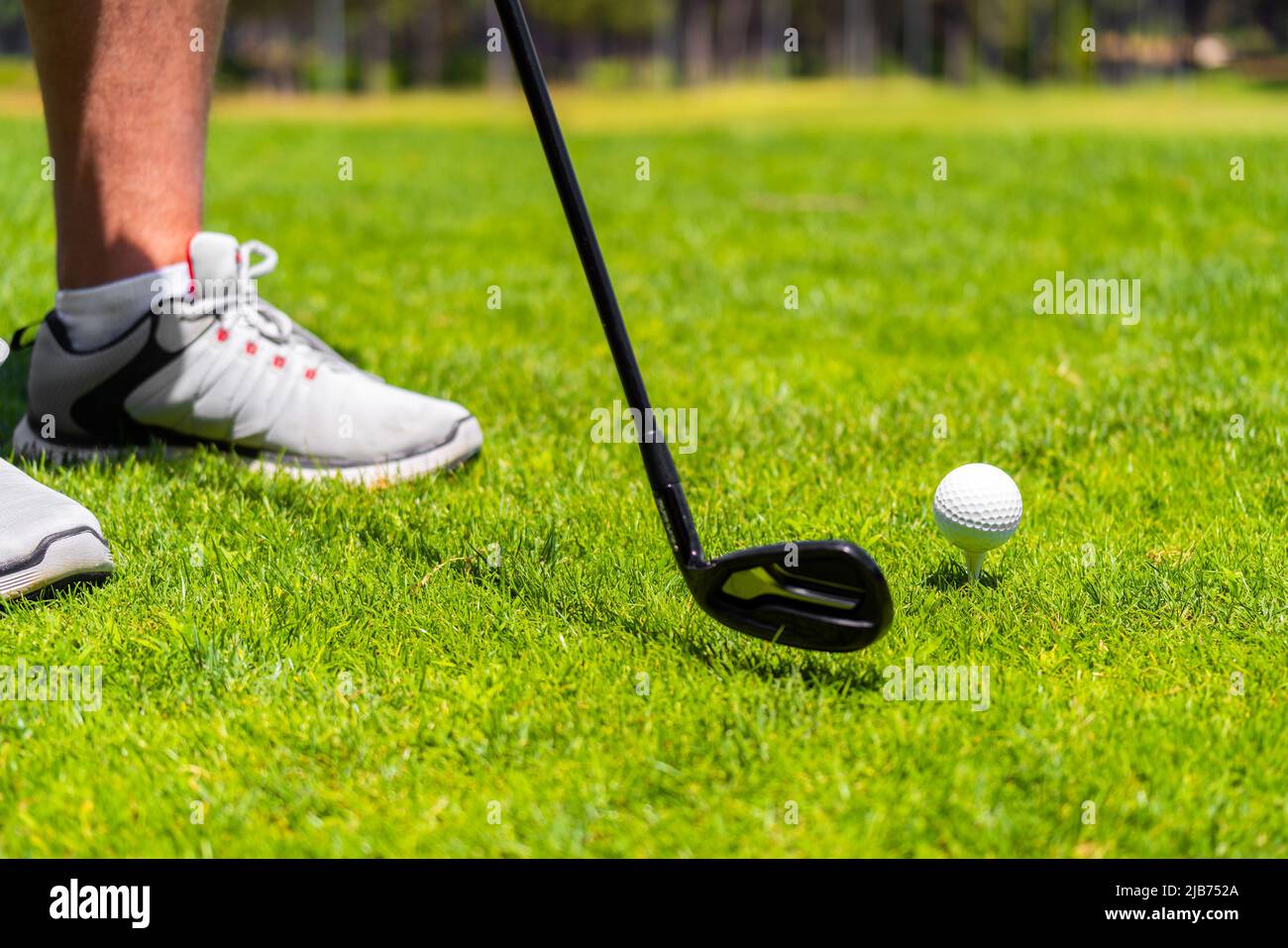 Mann, der mit einem eisernen Golfschläger steht, bereit, auf dem Golfplatz einen Ball auf grünem Gras zu schlagen Stockfoto