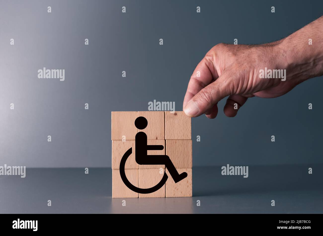 Konzept der Gleichheit für behinderte Menschen am Arbeitsplatz und im Leben. Handposierte Holzklotz mit Handicap-Symbol Stockfoto