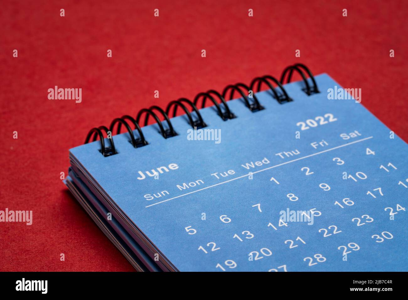 Juni 2022 - blauer Spiralkalender gegen rotes handgemachtes Papier, Zeit- und Geschäftskonzept Stockfoto