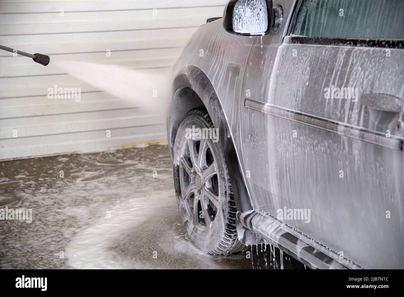 Ein Prozess der Spülung von SOAP sud auf silbernem Autorad mit druckbeaufschlagtem Wasserstrahl an der Self-Service-Autowaschstation Stockfoto
