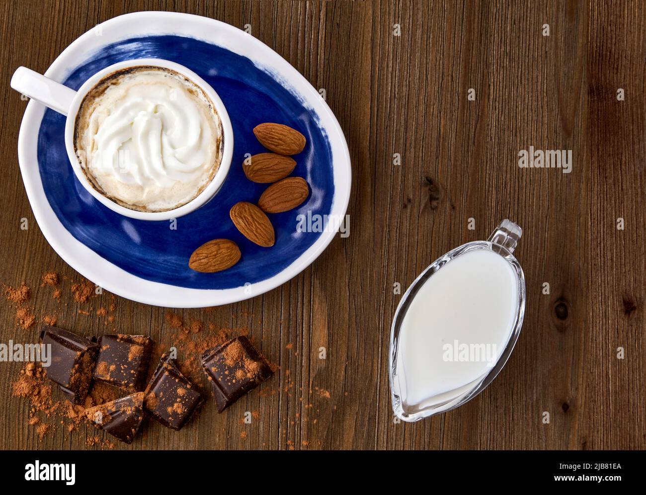 Blaue Tasse Kaffee mit Eis, Mandeln, Schokolade und Milch in einem Milchkännchen aus Glas auf einem dunklen Holztisch Stockfoto