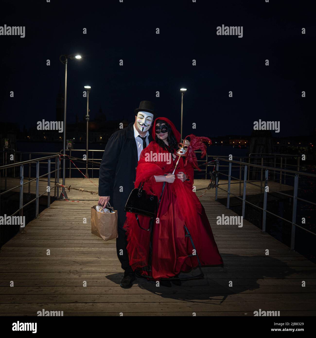 Venedig, Italien - 18.02.2022: Ein Mann und eine Frau in venezianischen Karnevalskostümen stehen nachts auf dem hölzernen Pier am Canal Grande in Venedig Stockfoto