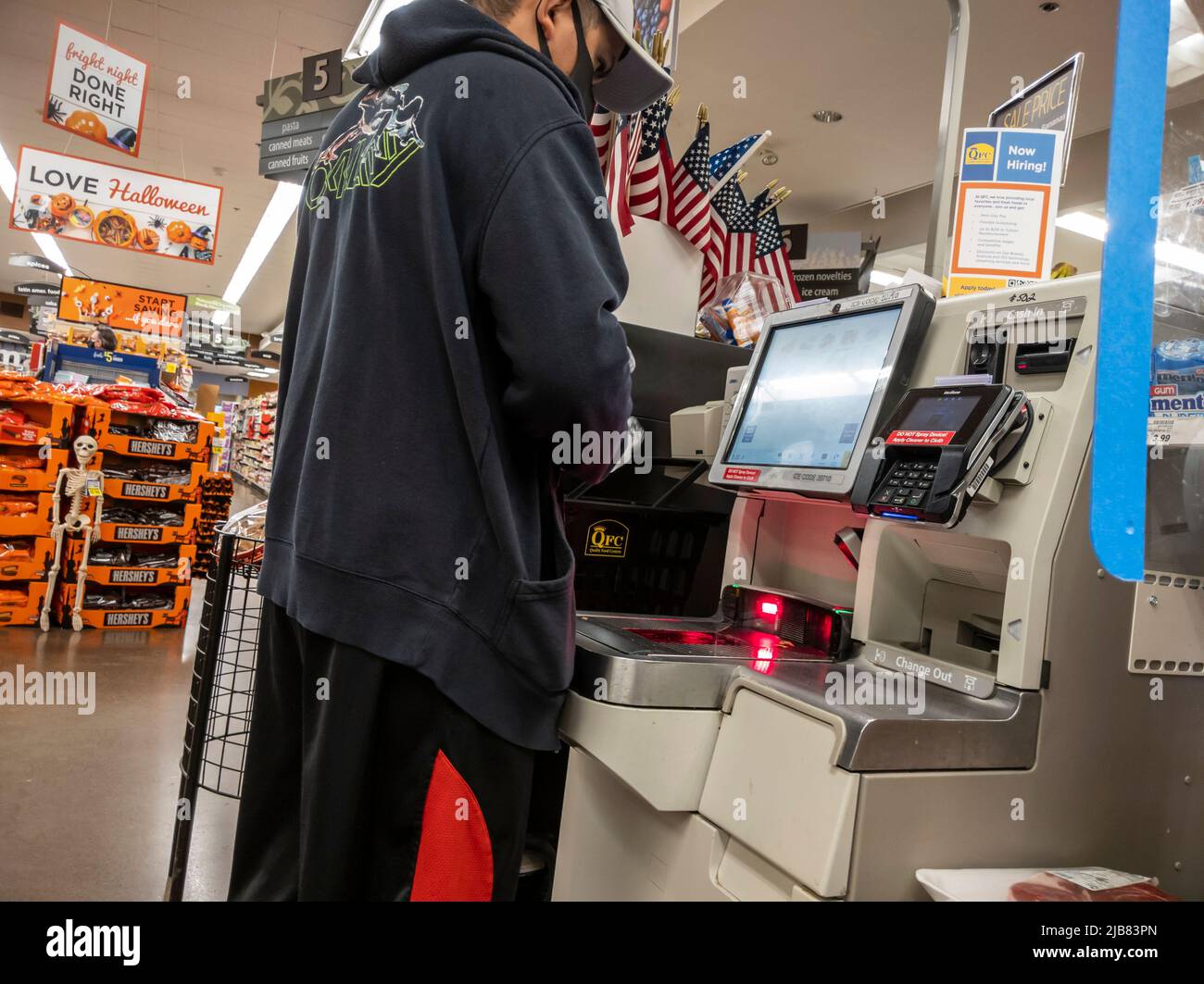 Kirkland, WA USA - ca. September 2021: Schräge Ansicht eines Mannes mit Gesichtsmaske, der an einem Selbstbedienungsautomaten in einem QFC-Lebensmittelgeschäft auscheckt. Stockfoto