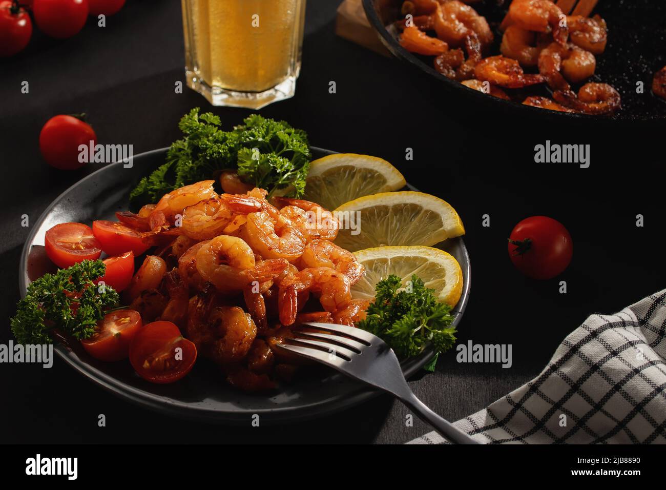 Abendessen serviert: Gebratene Garnelen mit Zitrone, Tomaten und Kräutern sowie Bier in einem Glas auf dem Tisch Stockfoto