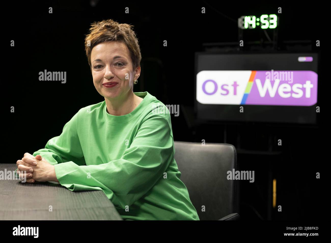 Berlin, Deutschland. 30.. Mai 2022. Maria Makeeva, Chefredakteurin bei  OstWest TV, sitzt in einem Studio, während das Senderlogo auf einem Monitor  im Hintergrund zu sehen ist. Der private Fernsehsender mit Sitz in