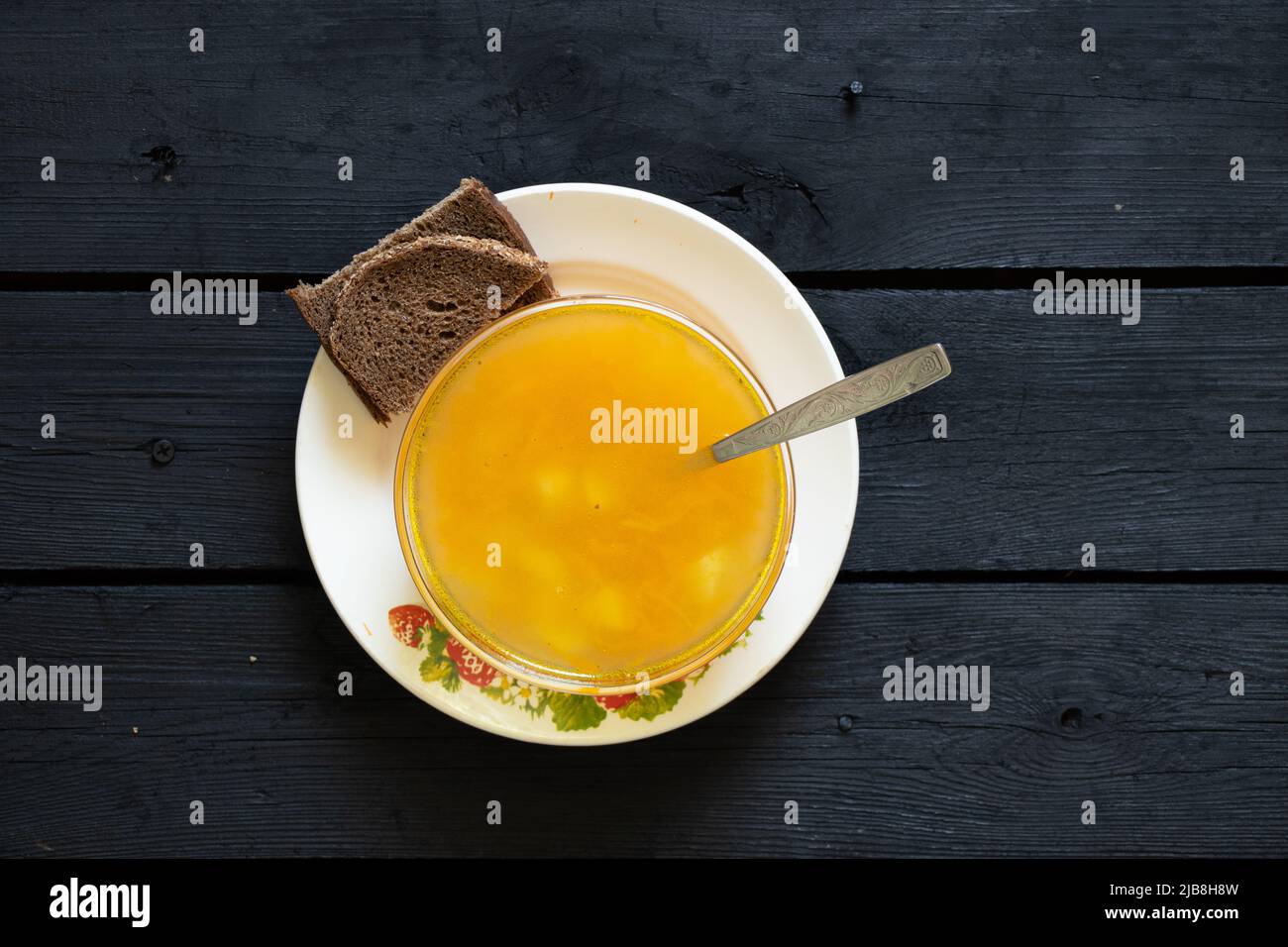 Gemüsesuppe und eine Scheibe Schwarzbrot auf einem schwarzen Holztisch in der Küche, Suppe ohne Fleisch Stockfoto