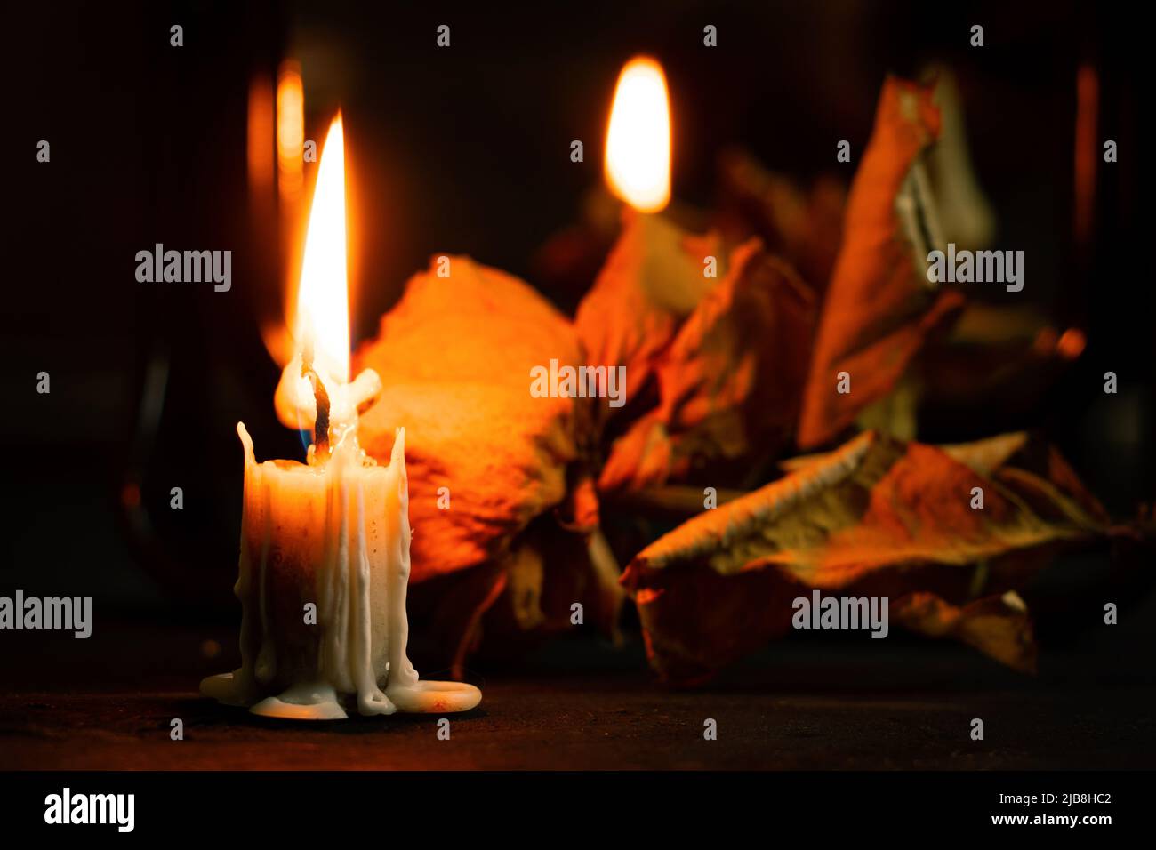 Brennende Kerze in der Nähe des Spiegels auf dem Tisch und daneben liegt eine trockene Rose im Dunkeln, Kerzenflamme in der Nacht, trauernd Stockfoto