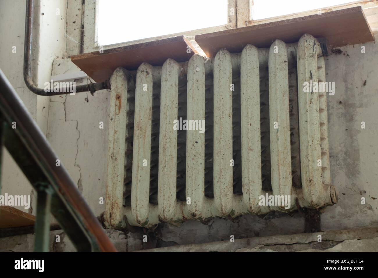 Eine alte rostige gusseiserne Batterie hob die Fenster am Eingang eines mehrstöckigen Gebäudes in der Ukraine an, heizte das Haus, die Batterie im Haus i Stockfoto