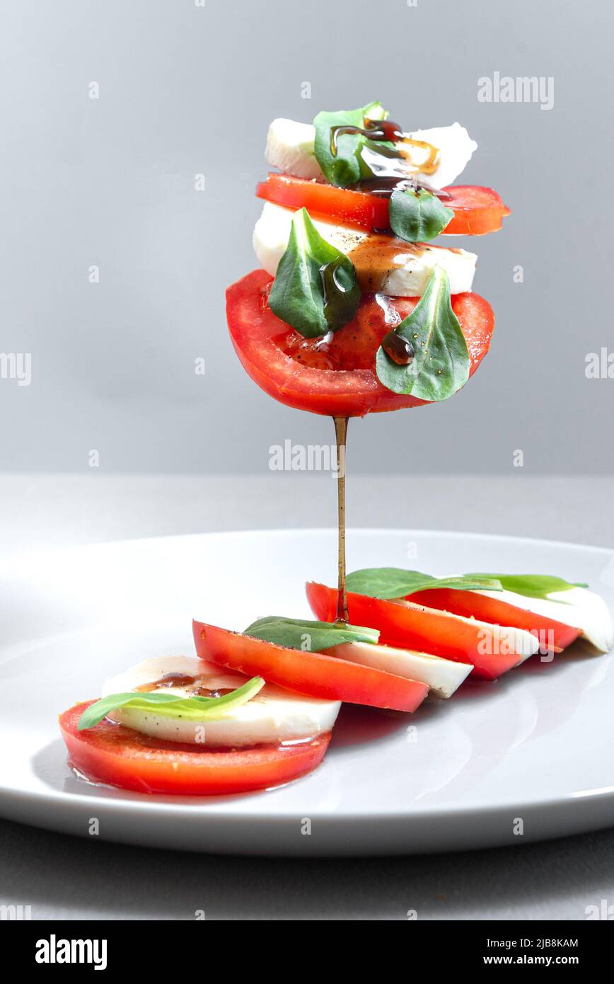 Italienischer Caprese-Salat mit geschnittenen Tomaten, Mozzarella, Basilikum, Olivenöl auf grauem Hintergrund. Fliegende Inridients. Italienischer Salat auf schwarzem Teller mit Stockfoto