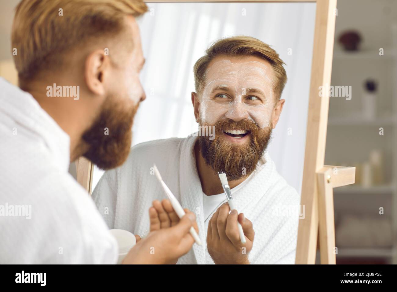 Nahaufnahme von lustigen Mann im Spiegel reflektiert, der kosmetische Maske für die Gesichtspflege anwendet. Stockfoto